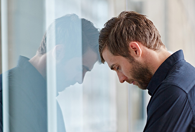 Man with head against a window feeling anxious