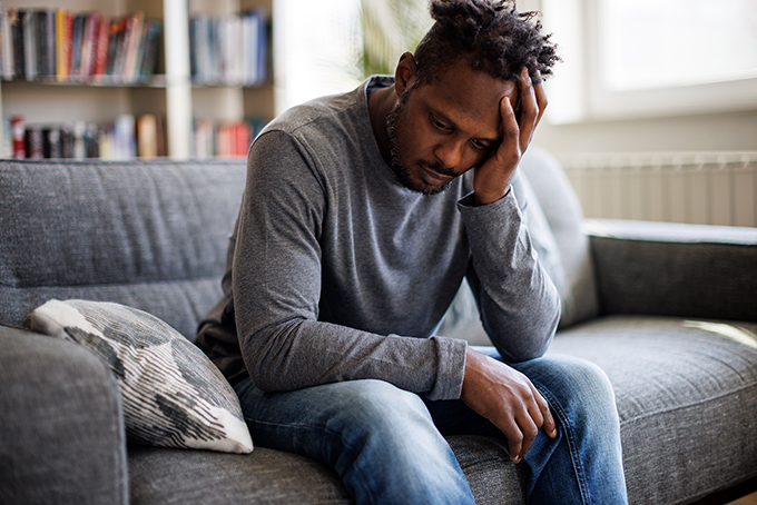 Man sitting at home looking stressed with head in hands thinking